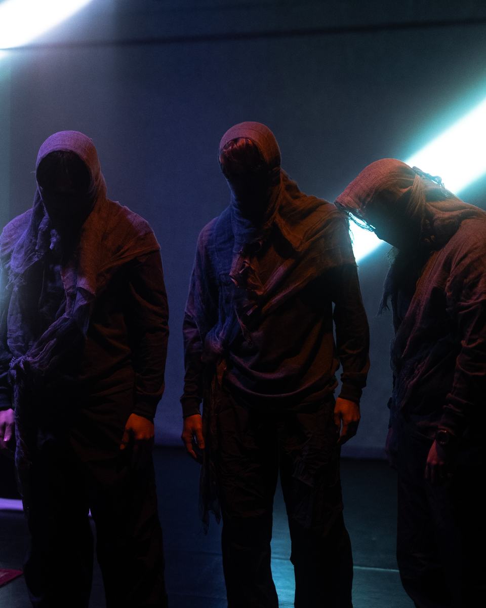 Three hooded dancers in teal light