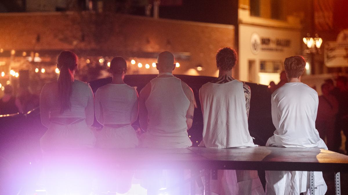 Five performers in white sitting on the edge of a platform