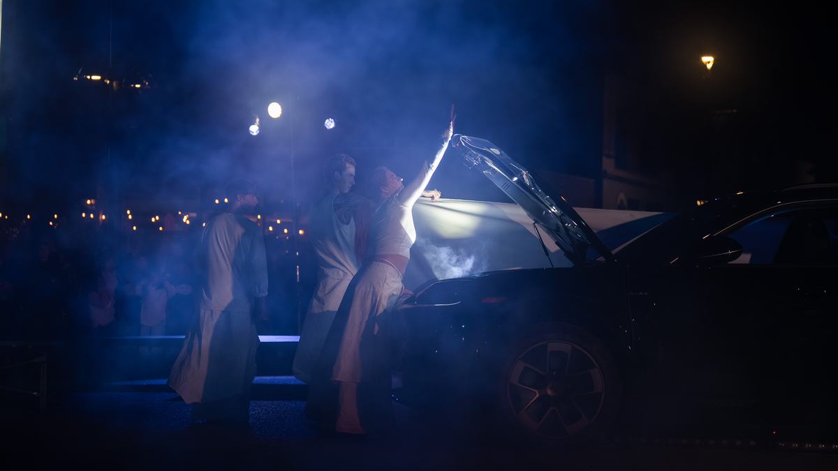 Dancers in blue haze at the open hood of the car